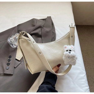 Detail of creamy white crescent shoulder bag featuring pleated leather and a puppy charm