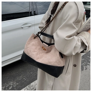 Detail of a large quilted tote bag with chain strap and gold clasp on a trench coat model