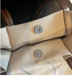 Detail of magnetic silver hardware on cream canvas and brown leather tote bag