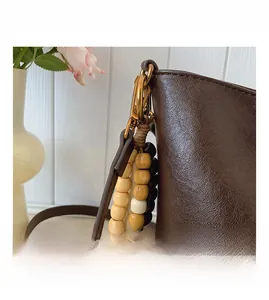 Détail du sac seau en cuir marron foncé avec attaches dorées et pendentif en perles de bois
