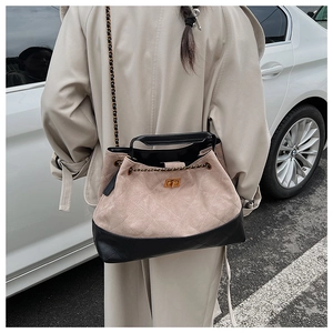 Detail of beige suede tote bag featuring black leather trim and gold chain strap decoration