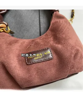 Detail of reddish brown suede hobo bag featuring dark leather tag and metal chain strap