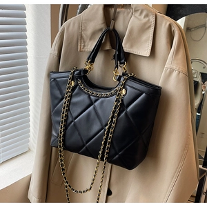 Detail of black quilted tote bag with matte leather finish and gold chain shoulder strap