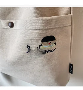 Detail of beige canvas tote featuring cartoon girl embroidery and Smile Girl text design