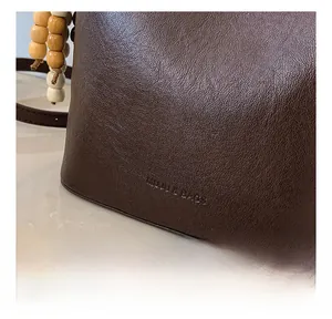 Détail d'un sac seau en cuir grainé marron avec lettrage MUJI et breloque en perles de bois
