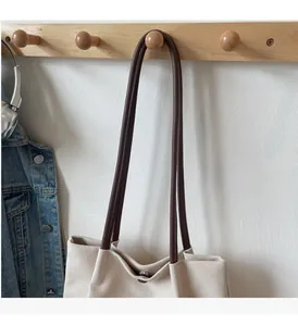Detail of beige canvas tote bag with brown leather handles and secure metal button closure