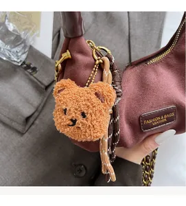 Detail of dark brown suede crescent bag with gold zipper and plush bear charm accessory