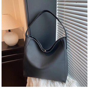 Detail of minimalist black faux leather tote bag with wide strap on a soft white fabric
