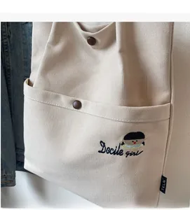 Detail of off-white canvas tote bag with Docile Girl embroidery and brown button pocket