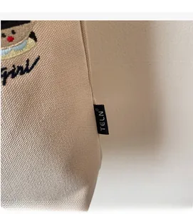 Detailed close-up of beige canvas bucket bag with logo tag and cartoon embroidery