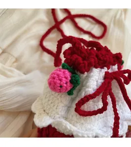 Close-up of handmade crochet bucket bag featuring red-white knit and strawberry charms