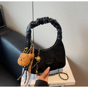 Detail of black suede dumpling bag with leather handle and cute brown bear charm