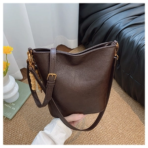 Détail d'un sac seau marron foncé avec logo embossé et breloque décorative en perles de bois