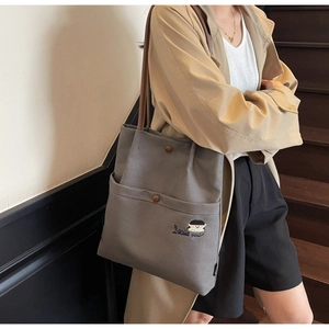 Detail of grey-blue canvas tote with brown leather strap and Docile girl embroidery