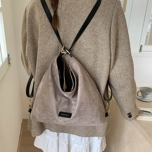 Detail of taupe suede bucket bag with adjustable black straps and fashion label