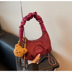 Detail view of burgundy suede dumpling bag with pleated handle and plush bear charm