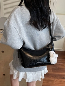 Fashionable black glossy pleated underarm bag with white teddy bear charm on model