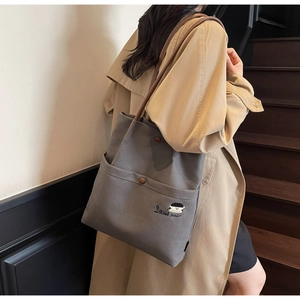 Detail of gray canvas tote with leather straps, retro button, and cute girl embroidery