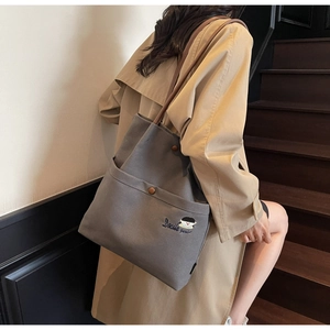 Detail of grey canvas tote bag featuring embroidered cartoon design and brown leather straps