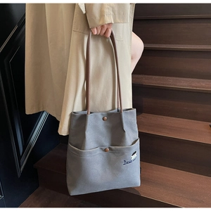 Detail of grey canvas tote bag with brown leather handles and Docile embroidery