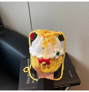 Detailed close-up of handmade yellow and white crochet bucket bag with knit strawberry charm