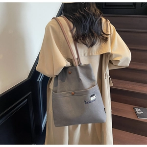 Detail of grey canvas tote bag with embroidered girl character and brown leather straps