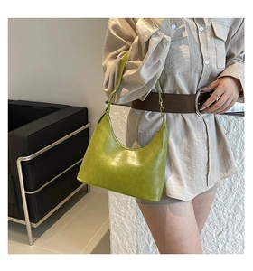 Close-up of a green crescent shoulder bag with glossy texture shown in a fashion setting
