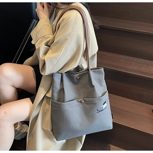 Detail of grey canvas tote bag with brown leather straps and Docile girl embroidery