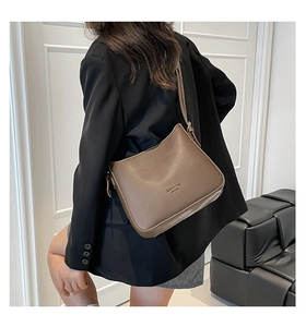 Detail view of the brown leather bucket bag with embossed logo on an adjustable shoulder strap