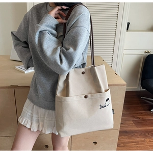 Detail of light beige canvas tote bag with brown strap and embroidered front pocket design