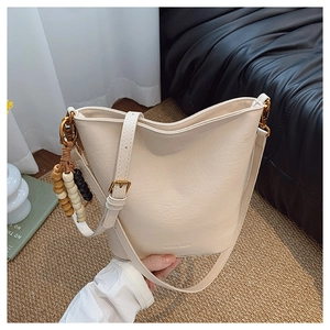 Détail du sac seau beige avec logo embossé et pendentif en perles de bois sur le côté
