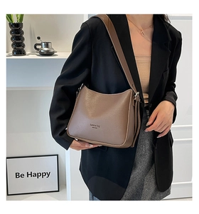 Brown faux leather shoulder bag with wide strap worn by a model in a minimalist setting