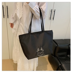 Detailed view of black canvas tote bag with white deer embroidery worn on shoulder
