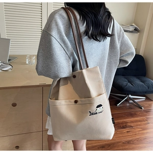 Detailed close-up of beige canvas tote bag featuring cute cartoon embroidery and brown straps