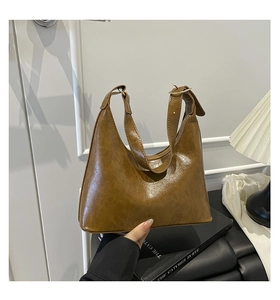 Detail view of brown glossy leather crescent bag with adjustable strap and metal buckle