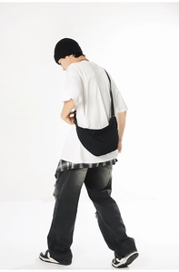 Side view of a black canvas crescent crossbody bag worn by a model in casual street style