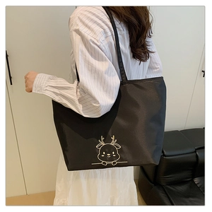 Detail of black tote bag with gold deer embroidery worn by model in minimalist setting