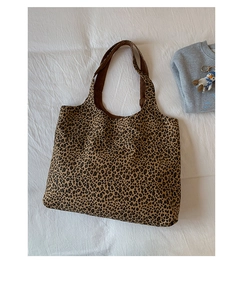 Flat lay of a leopard print tote bag with a penguin keychain on a white fabric surface
