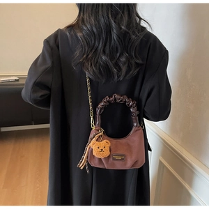 Detail of a dark brown crescent bag with a plush bear charm and gold chain strap