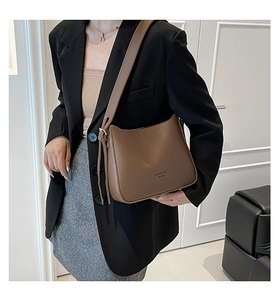 Brown leather crossbody bag with New York text detail shown on person in a modern interior