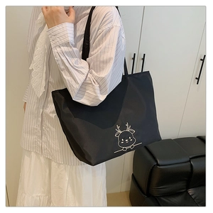 Detail of black tote bag with white deer embroidery shown on a shoulder model