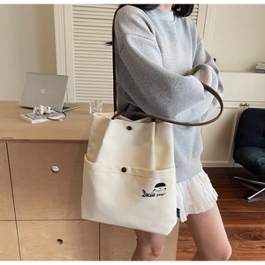 Detail of cream canvas tote bag with brown straps and cute embroidered character design