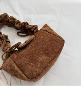 Close-up of brown suede crossbody bag featuring pleated strap and soft texture details