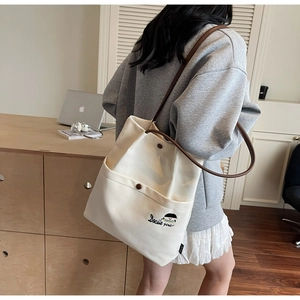 Detail of beige canvas tote bag featuring brown leather straps and girl embroidery