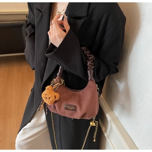 Detail of retro brown crescent bag with pleated handle, chain strap and plush bear charm
