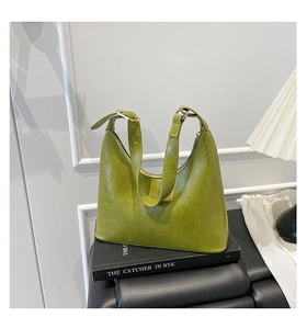 Close-up of avocado green leather hobo bag with adjustable strap on a book background