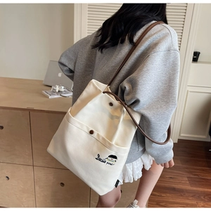 Detail of canvas tote bag featuring Docile Girl embroidery and brown leather shoulder strap