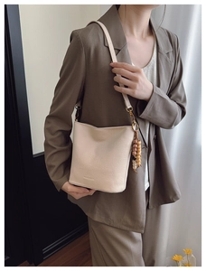 Détail d'un sac seau crème avec pendentif en perles, porté à l'épaule par un mannequin