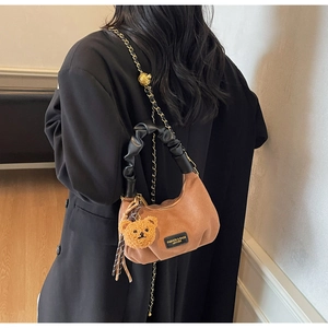 Detail of brown suede crescent bag featuring a pleated handle and plush bear charm accessory