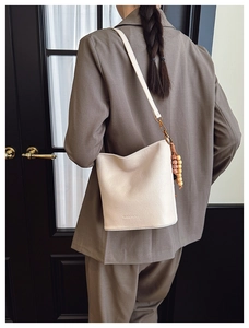 Sac seau beige avec perles en bois porté par un mannequin en blazer marron chic